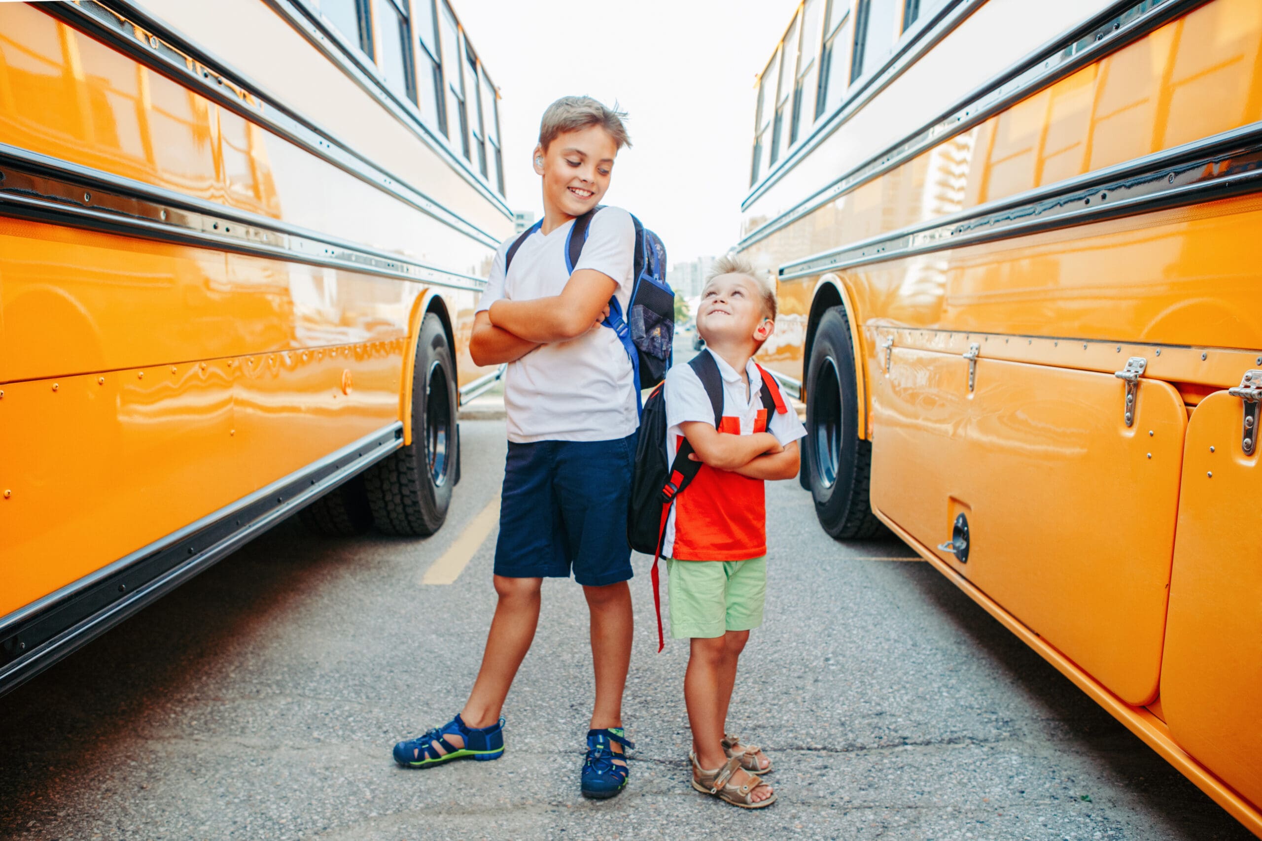 two children posing between two school buses
